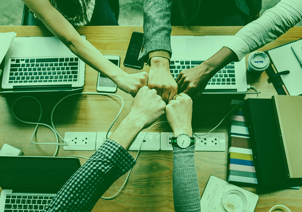 A team of app developers in New York collaborating with a fist bump over laptops, symbolizing teamwork and project success.